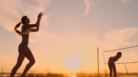 Eine-Schöne-Frau-Im-Bikini-Mit-Einem-Ball-Macht-Sich-Bei-Sonnenuntergang-Bereit,-Bei-Einem-Volleyballspiel-Im-Sand-Am-Strand-Einen-Aufschlagsprung-Zu-Machen.-Der-Entscheidende-Moment,-Der-Spannende-Moment-Des-Spiels-In-Zeitlupe.